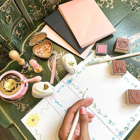 Someone writing a note at a desk surrounded by writing accessories