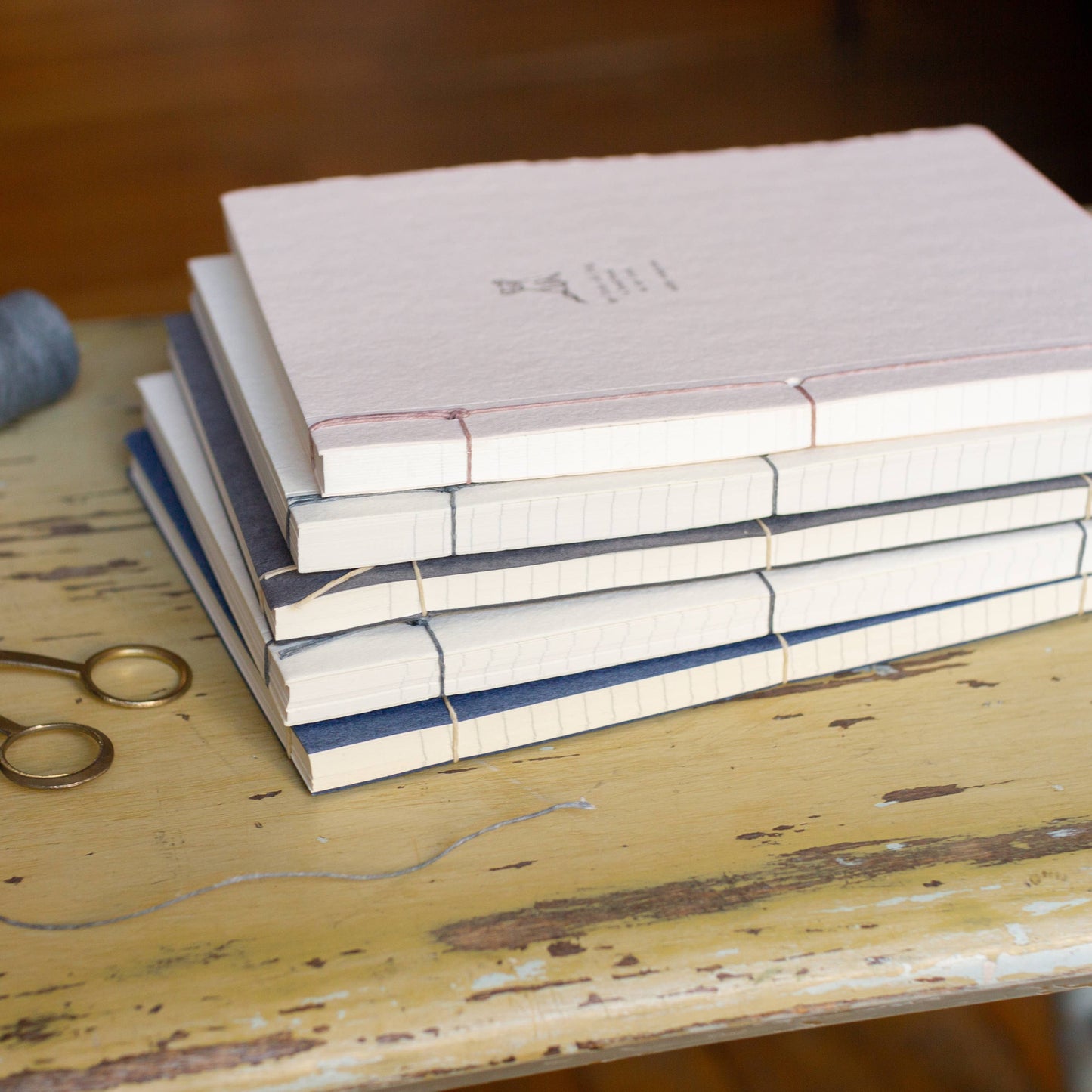 Stack of books on a wooden surface with a spool of thread and scissors.