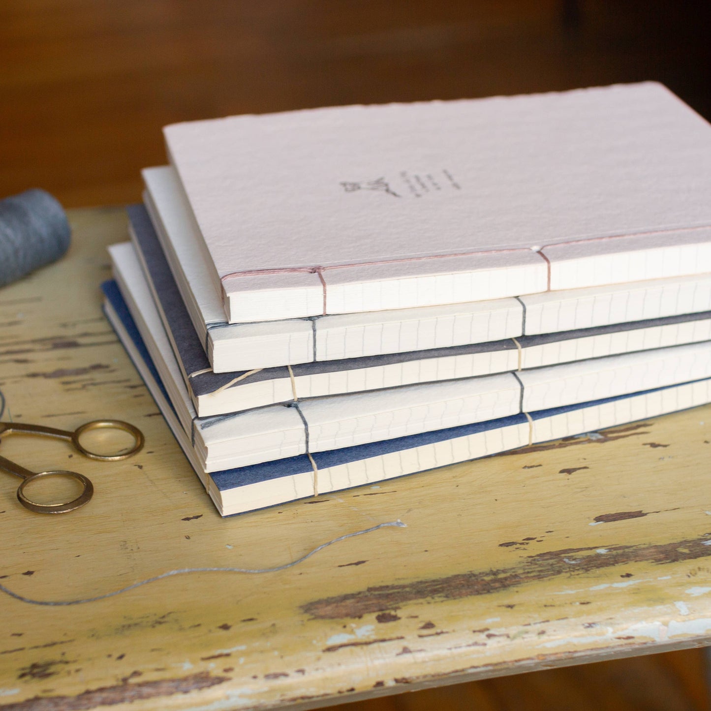 Stack of books on a wooden surface with a spool of thread and scissors.