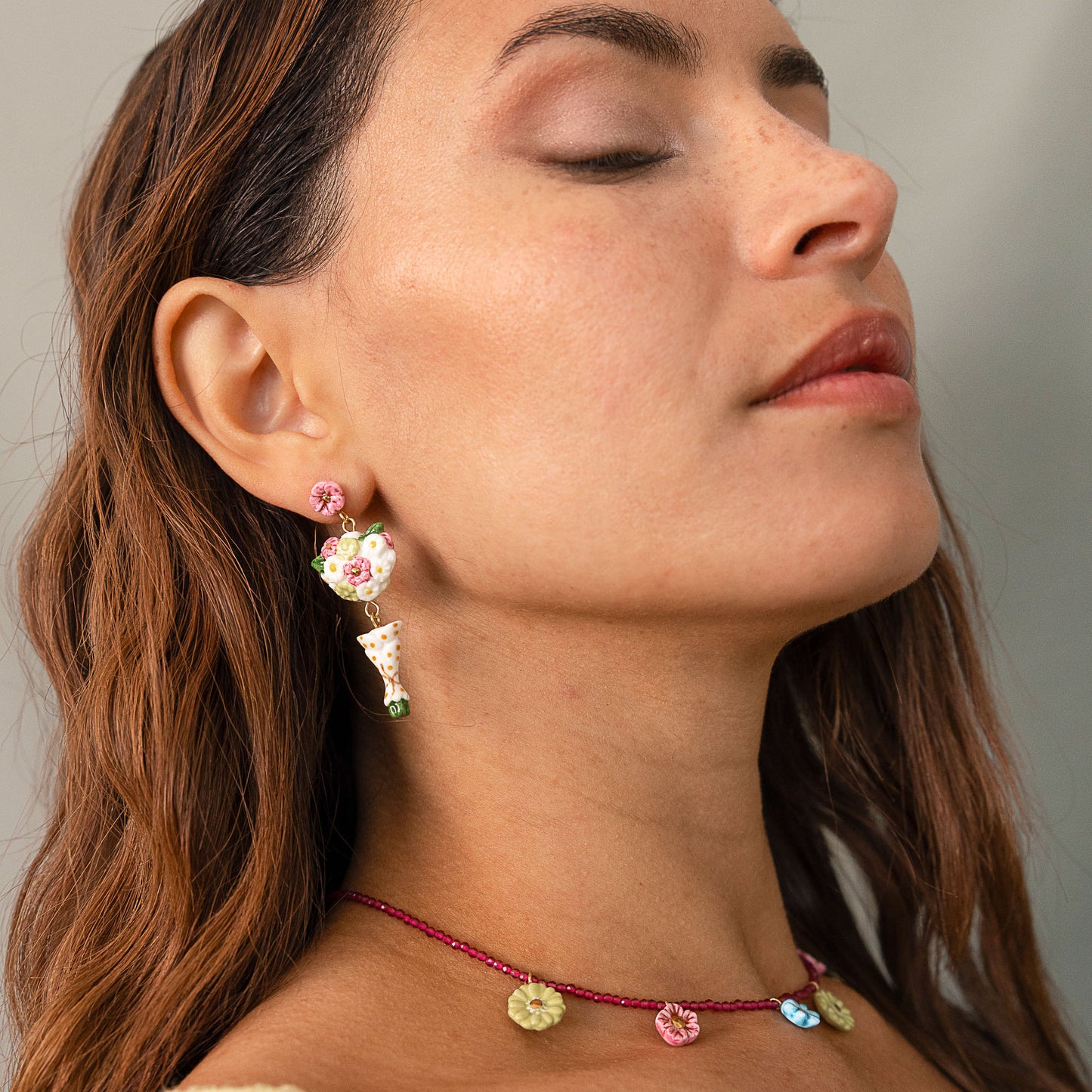 Close-up of a woman wearing colorful earrings and a necklace with a neutral background