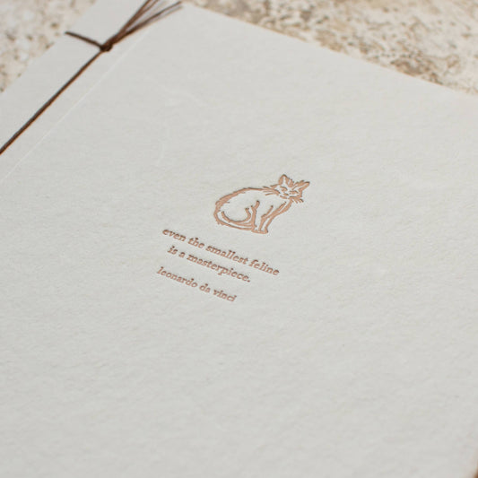 White notebook with gold text and cat illustration on a textured surface