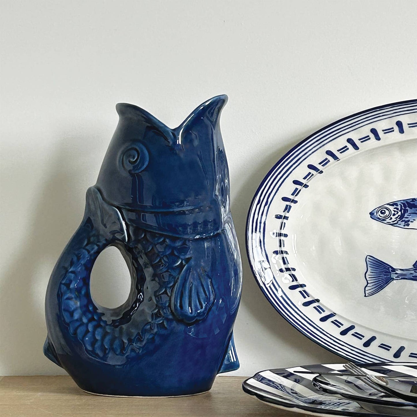 Blue ceramic fish-shaped object next to a white plate with blue fish design on a light background