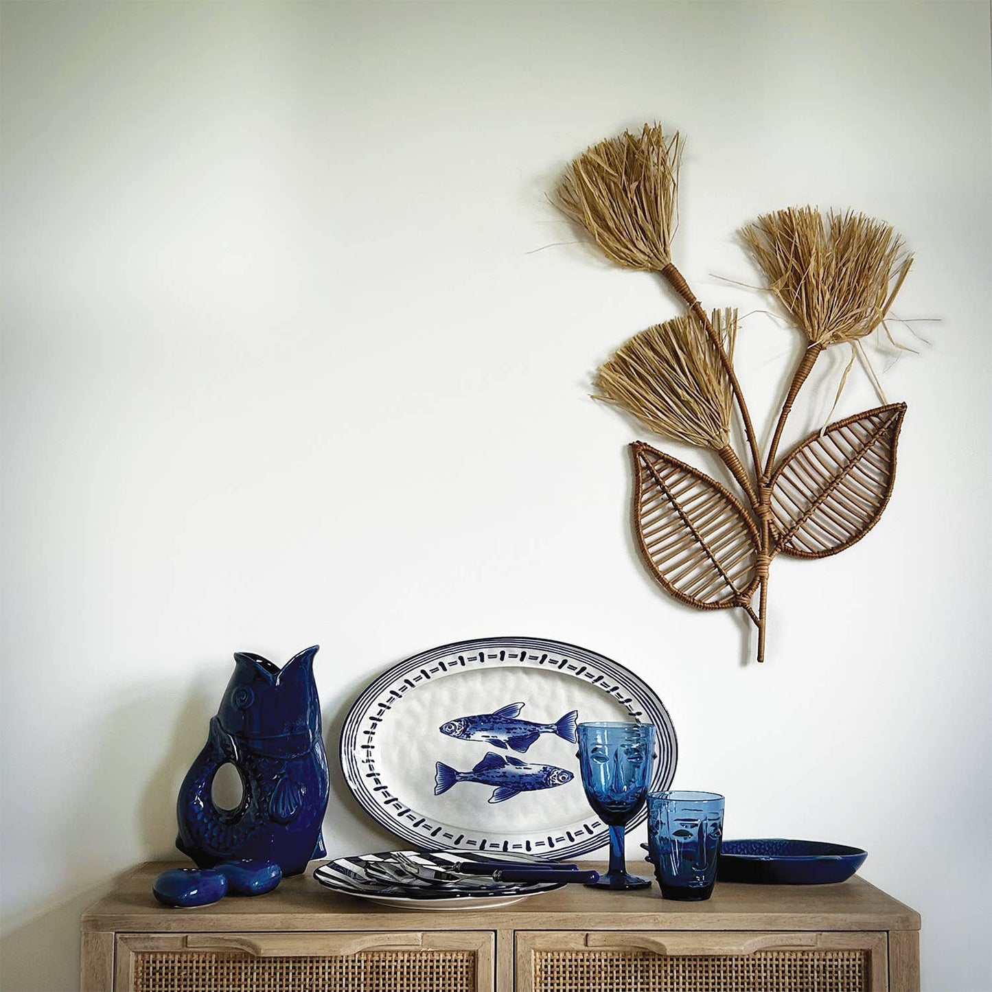 Decorative items including a blue owl figurine, ceramic plates with fish design, and a woven plant wall art on a wooden cabinet.