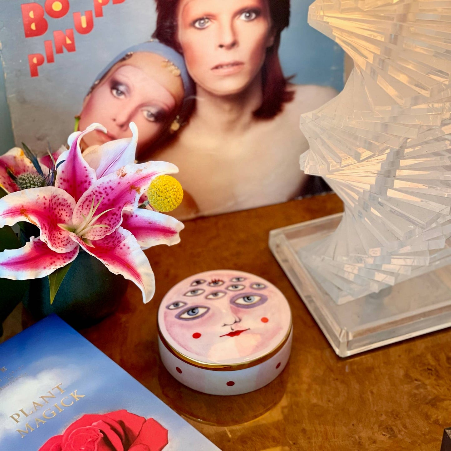 Vintage-style product with decorative lid on a wooden surface, featuring a book and flowers.