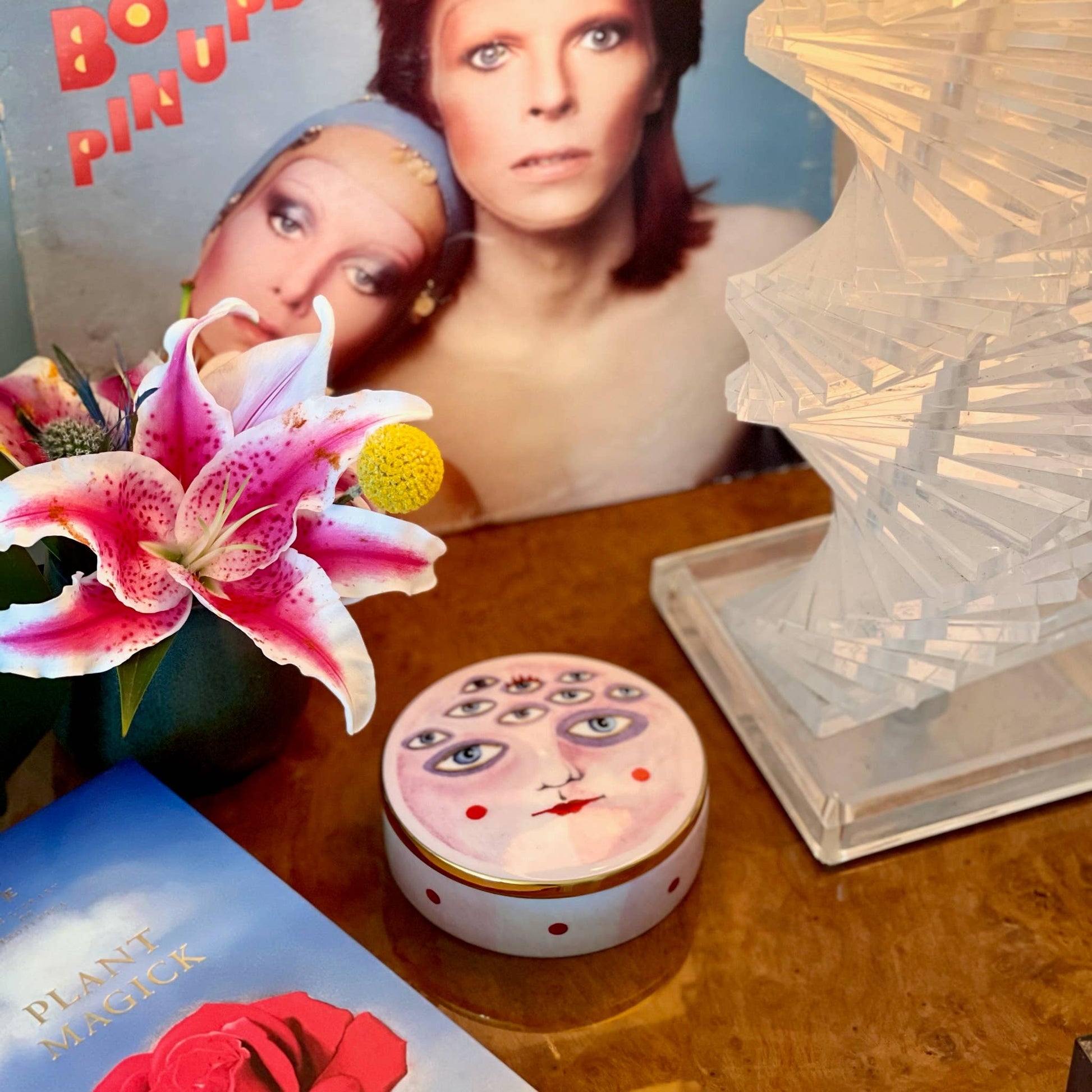 Vintage-style product with decorative lid on a wooden surface, featuring a book and flowers.