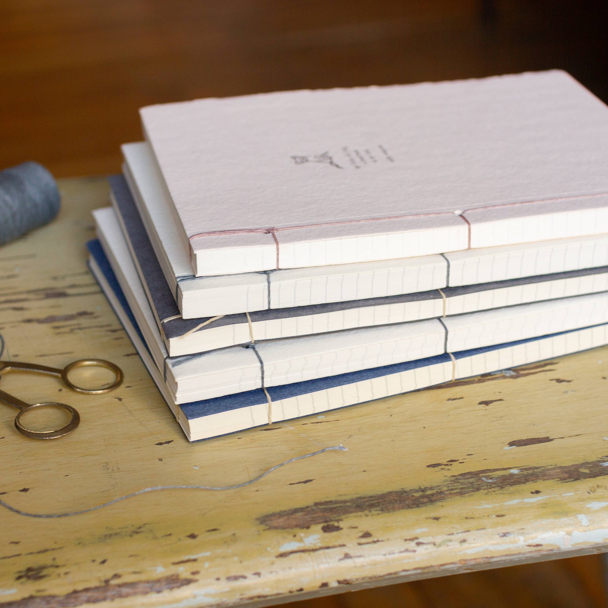Stack of books on a wooden surface with a spool of thread and scissors.