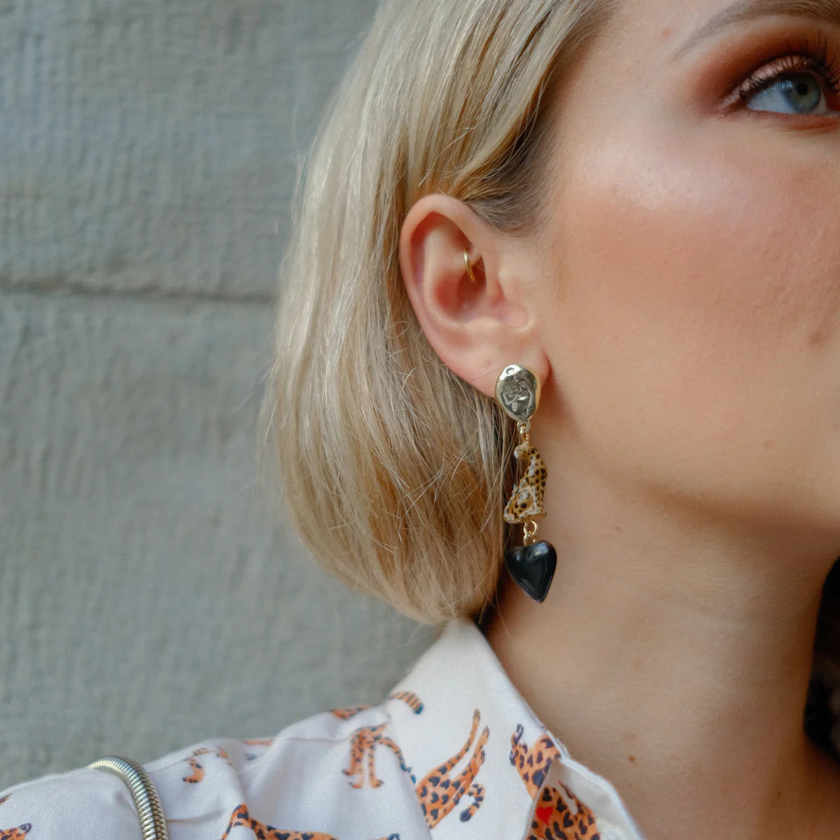 Close-up of a person wearing a dangling earring with heart-shaped charms against a neutral background.