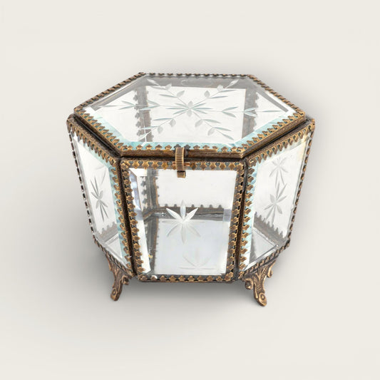 Hexagonal glass box with ornate brass trim on a light gray background