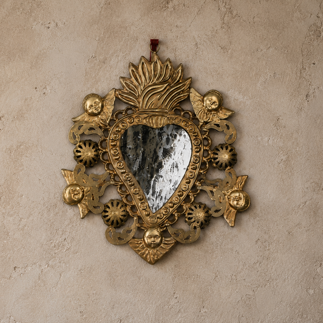 Decorative gold heart-shaped mirror with intricate designs on a beige wall.