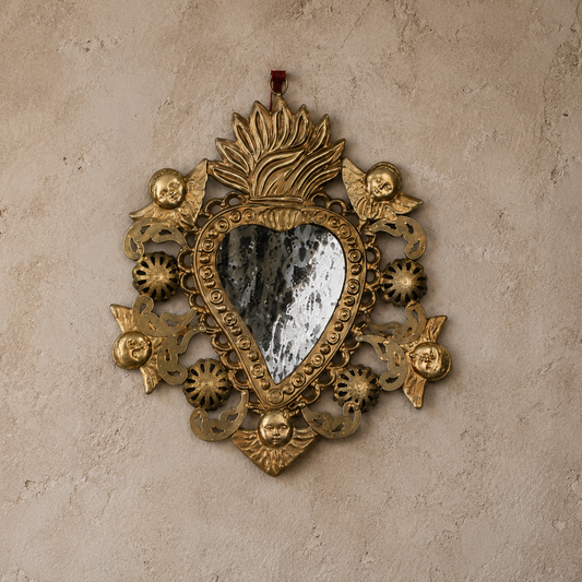 Decorative gold heart-shaped mirror with intricate designs on a beige wall.