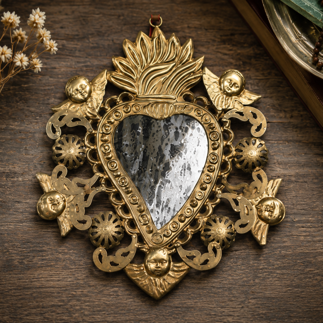 Decorative gold heart-shaped pendant on a wooden surface with dried flowers and books.