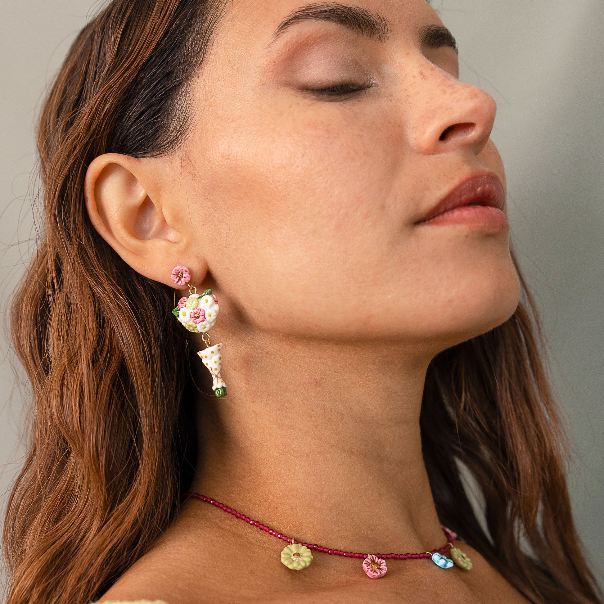 Close-up of a woman wearing colorful earrings and a necklace with a neutral background