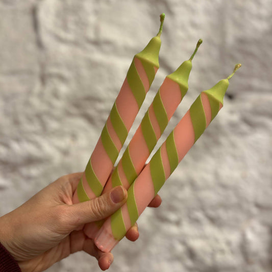 Hand holding two pink and green striped candles against a textured gray background