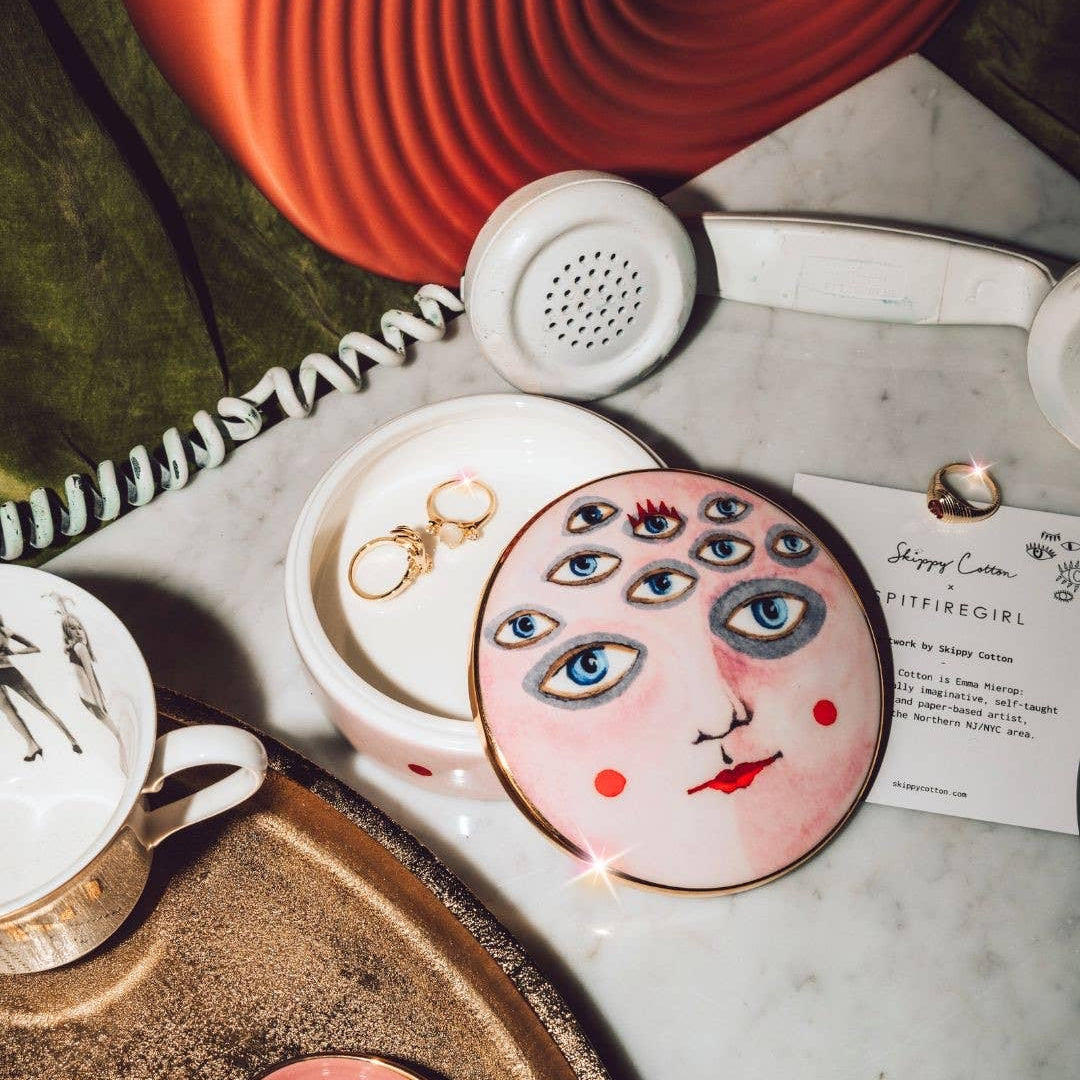 Makeup compact with artistic design on a marble surface with a phone and cup in the background.