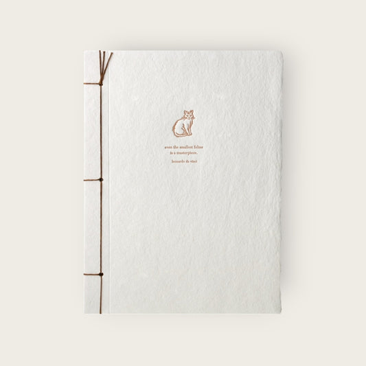 White notebook with brown binding and a cat illustration on a light beige background